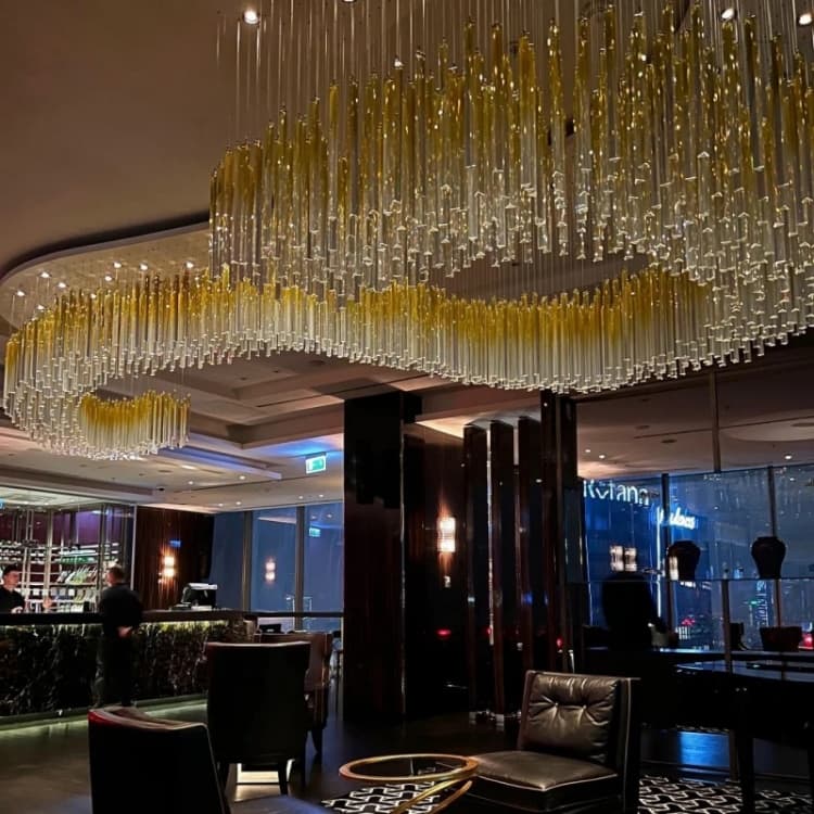 Gold-tone wave fixture with vertical clear rods above lounge seating